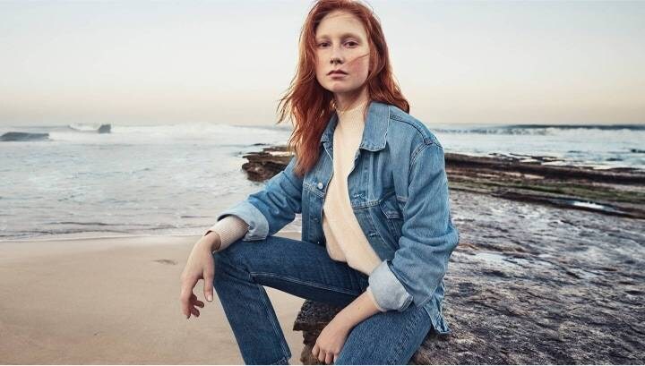 Woman sitting on the beach with the ocean behind her.